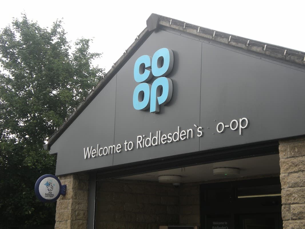 Co-op Food sign with "Welcome to Riddlesden's o-op" at a grocer's entrance, surrounded by greenery.