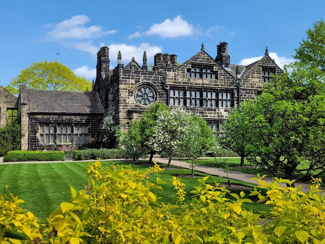 Historic East Riddlesden Hall features stone architecture, lush gardens, and a bright blue sky.