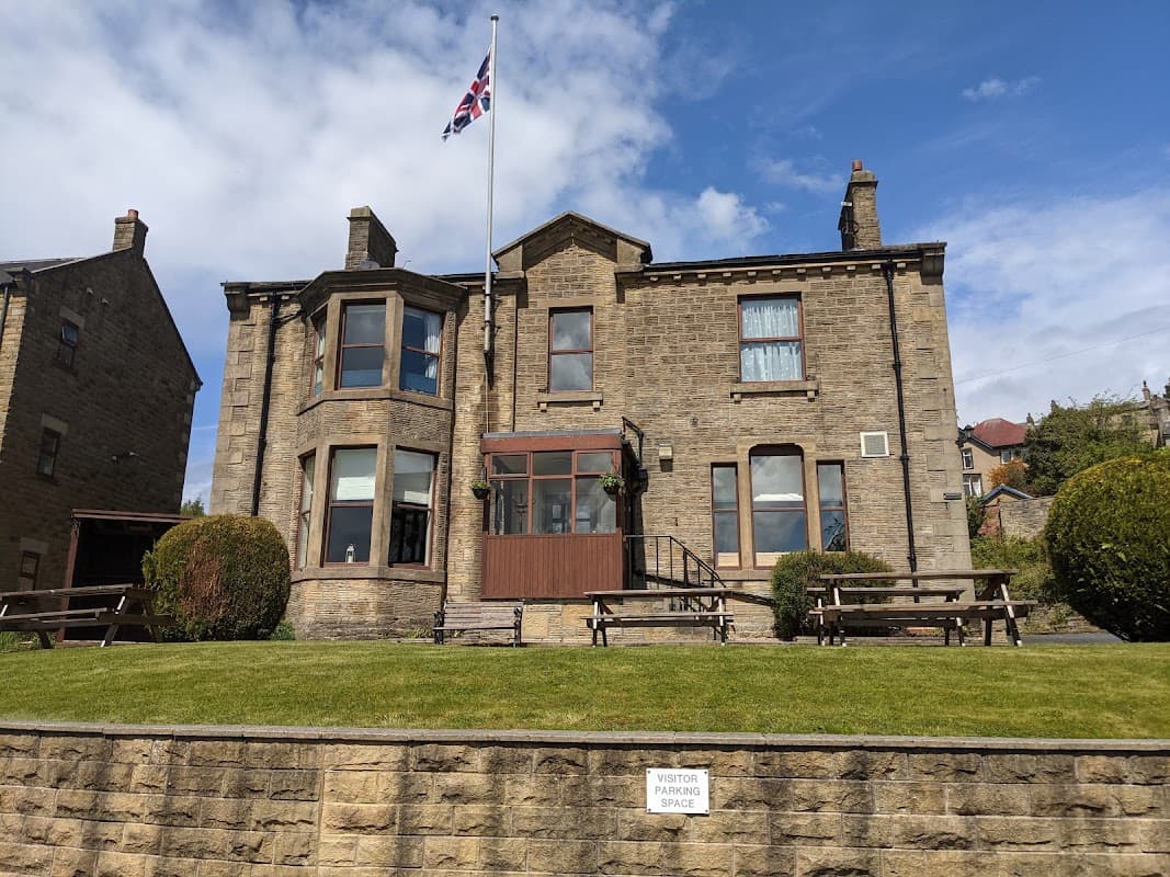Historic stone building with a Union Jack flag, surrounded by green lawn and benches, in Riddlesden, Yorkshire.