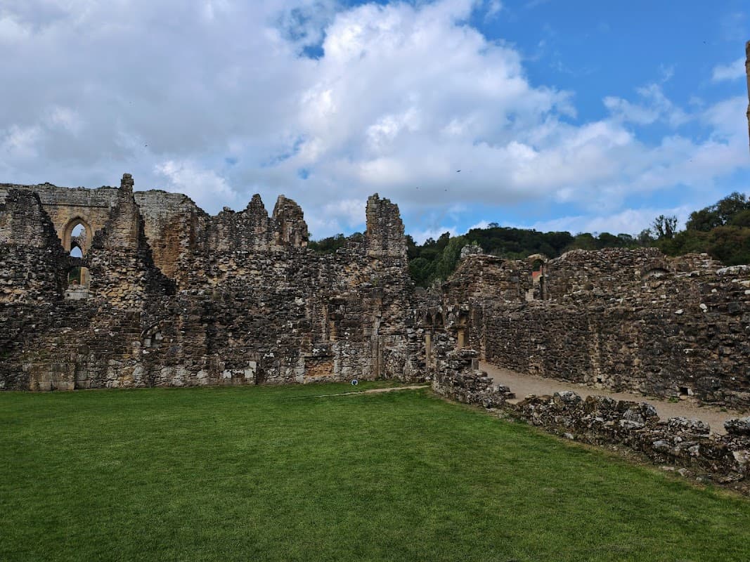 Ruins of Rievaulx Abbey with stone walls, grassy areas, and a partly cloudy sky in Yorkshire.