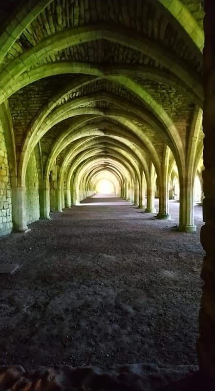 Arched stone columns create a shadowy corridor leading to bright light at the end, surrounded by textured walls.