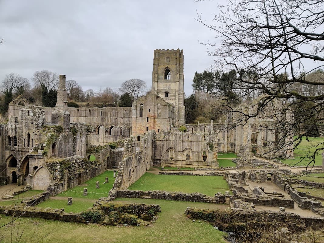 Ruins of Fountains Abbey with stone walls, archways, and grassy areas under a cloudy sky in Ripon, Yorkshire.