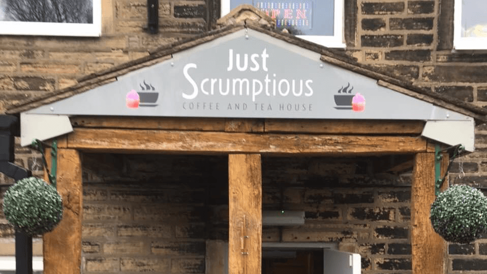 Sign for "Just Scrumptious" Coffee and Tea House with decorative hanging planters, set against a stone building.