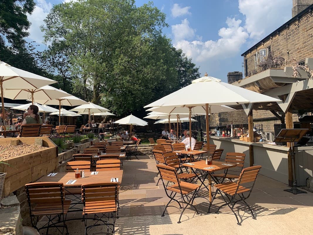 Outdoor bar area at The Malthouse in Rishworth, featuring wooden tables, umbrellas, and lush greenery.
