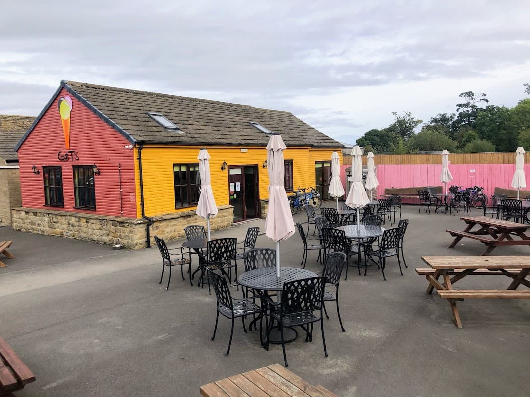 Brightly colored ice cream shop with outdoor seating and umbrellas, surrounded by a spacious patio in Risplith, Yorkshire.