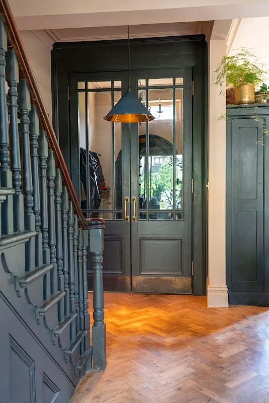 Elegant entrance with double doors, a pendant light, and a wooden staircase leading to a herringbone floor.