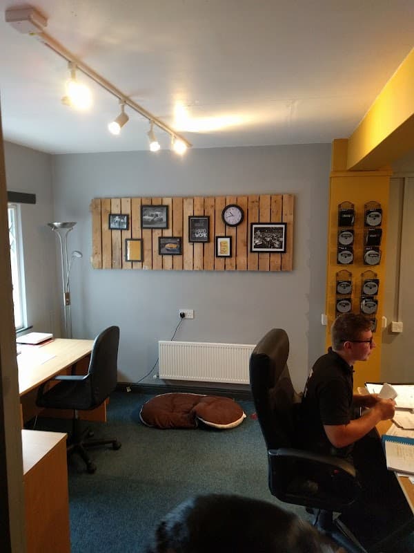 Modern office space with wooden wall decor, a clock, two desks, and a cozy pet bed on the carpeted floor.