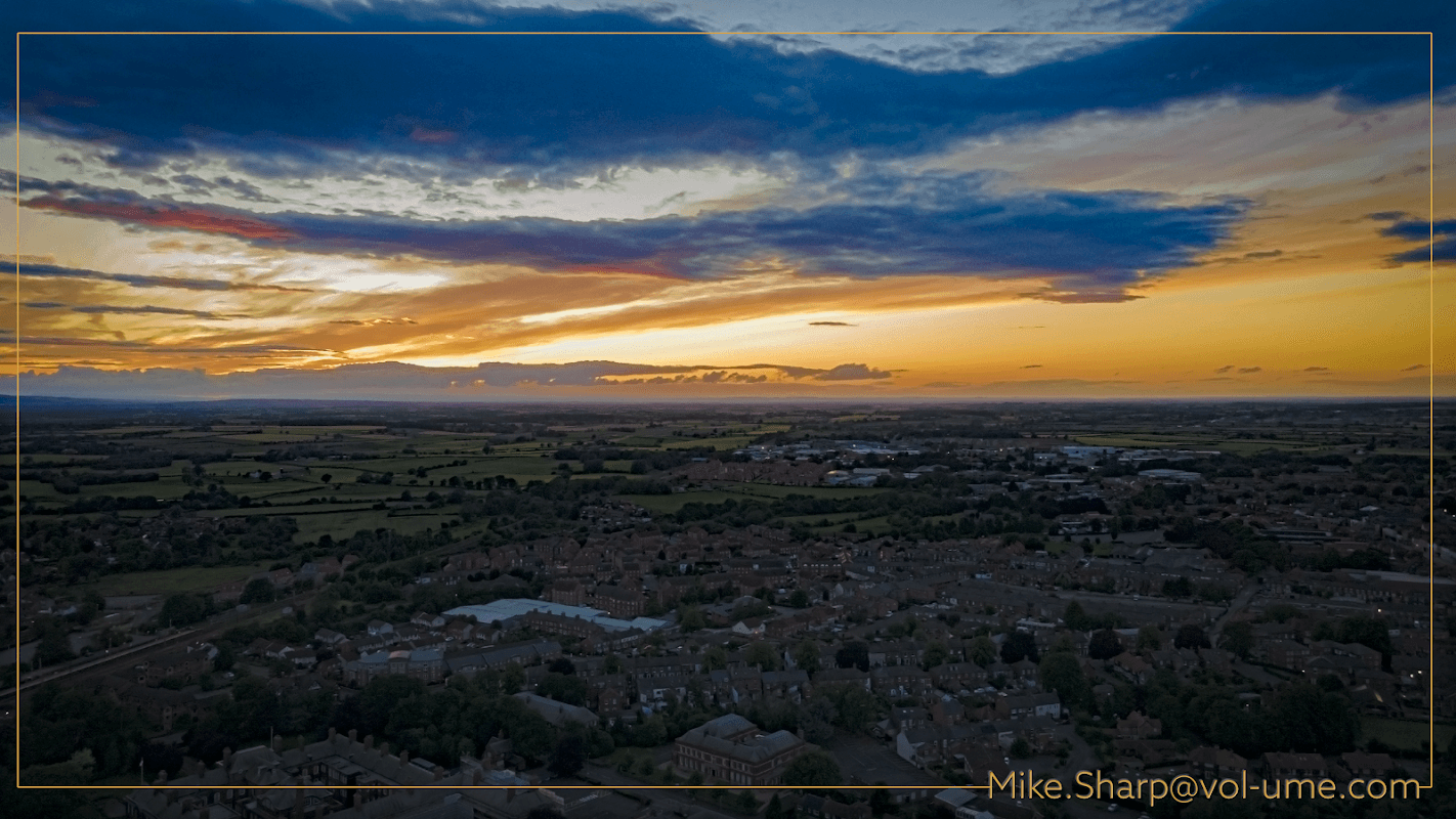 Colorful sunset over fields and rooftops in Romanby, Yorkshire, with a vast sky filled with clouds.