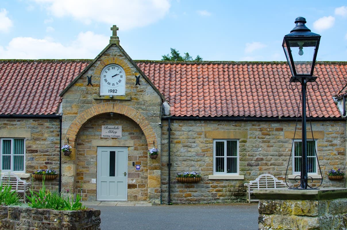Stone building with a clock, date 1992, and flower baskets, alongside a traditional lamppost and benches.