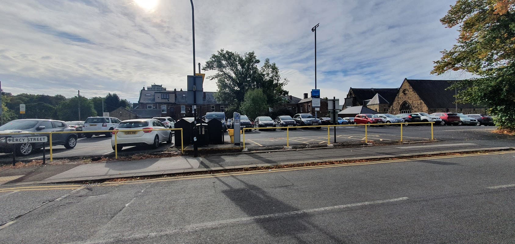 Clifton Hall Car Park with parked cars, yellow barriers, and nearby buildings under a partly cloudy sky.