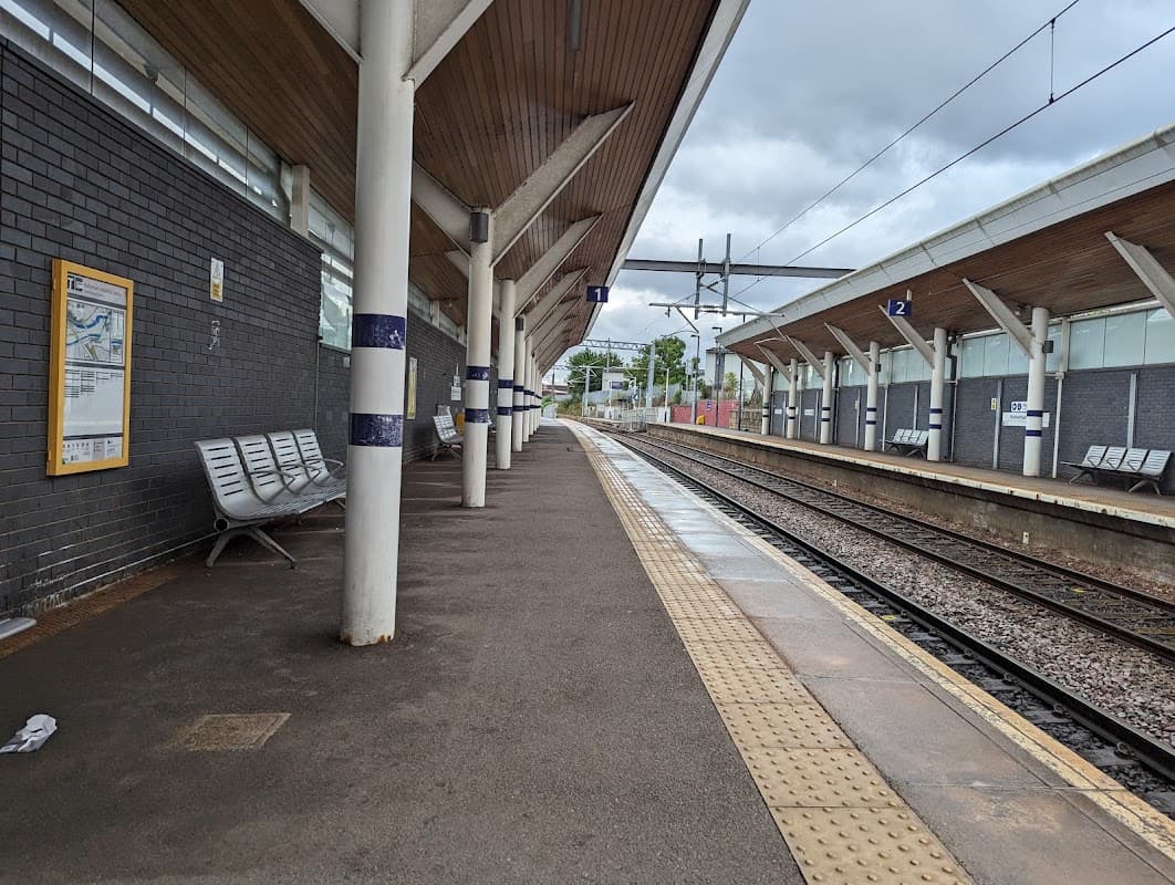 Platform at Rotherham Central station with benches, track, and overhead railway structures under a cloudy sky.