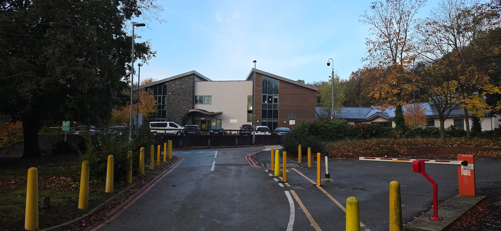 Rotherham Hospital staff car park entrance with pay & display, yellow bollards, and autumn trees in the background.