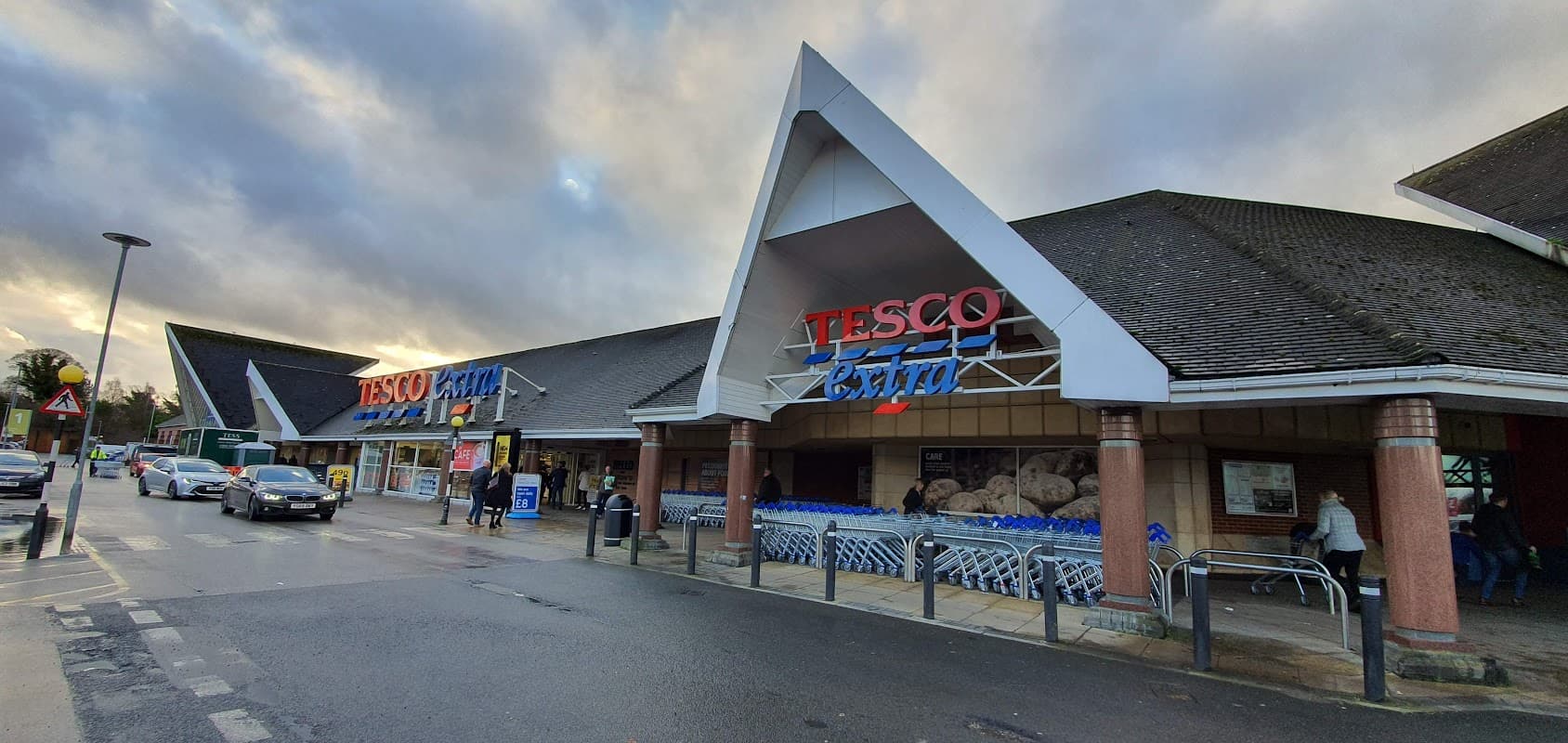 Tesco Extra store entrance with shopping carts outside, cloudy sky, and cars parked nearby in Rotherham, Yorkshire.
