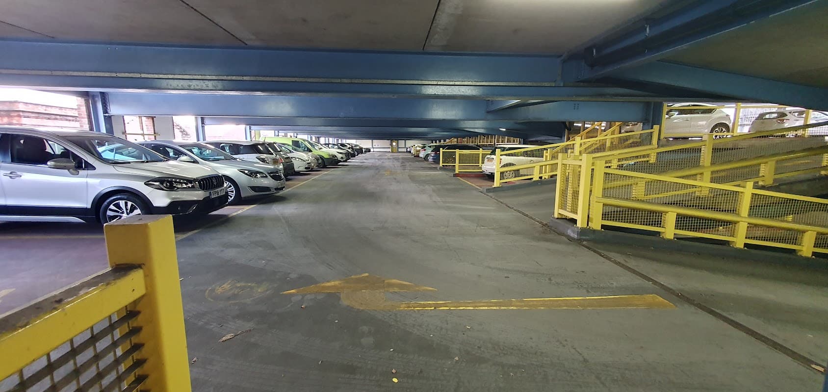 Multi-storey car park with parked cars, yellow barriers, and directional arrows on the ground in Rotherham, Yorkshire.
