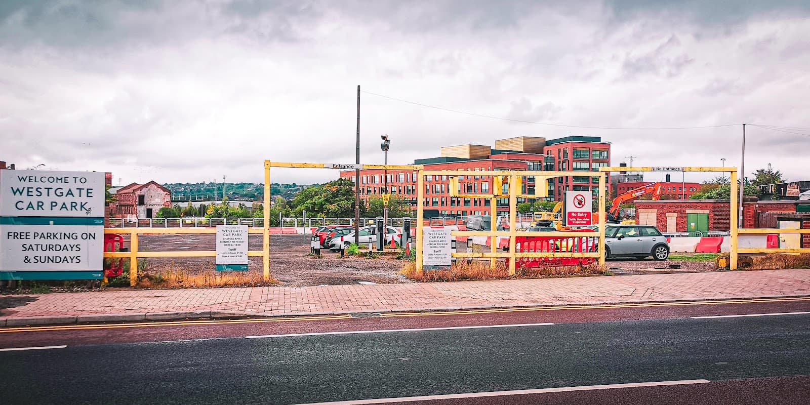 Welcome sign for Westgate Car Park with barriers, parking spaces, and buildings in the background on a cloudy day.