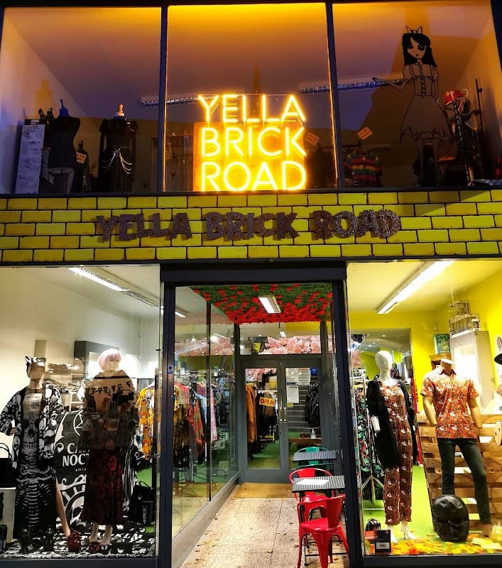 Brightly lit storefront with "YELLA BRICK ROAD" sign, colorful clothing displays, and vibrant decor.