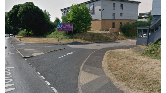 Pay & Display sign for "YourParkingSpace" near a road, with grassy areas and a building in the background.