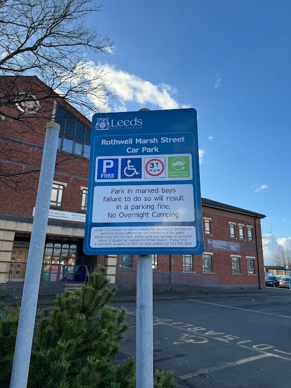 Rothwell Marsh Street Car Park sign with parking regulations, blue sky, and nearby brick building.