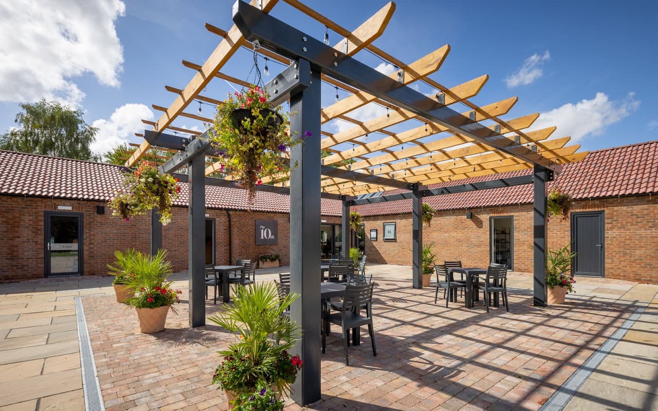 Outdoor cafe area with a wooden pergola, potted plants, and tables under a blue sky at High Farm Holiday Park.