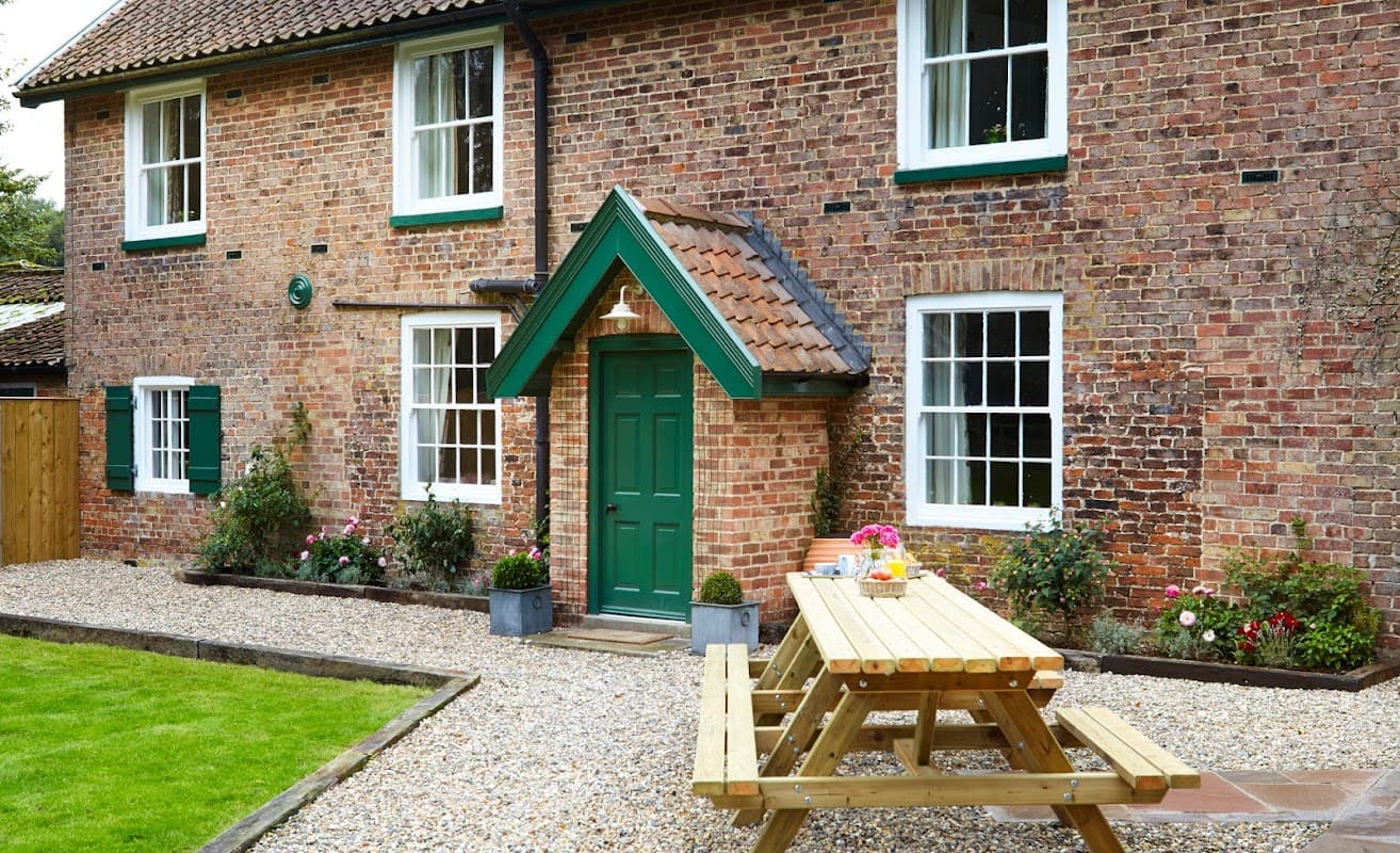 Brick cottage with green door, picnic table, and flower beds in a gravel yard at Thorpe Hall Cottages, Rudston.