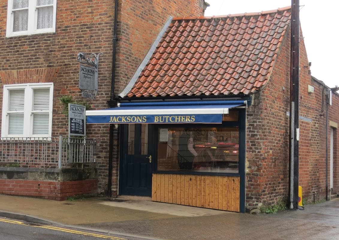 Shopfront with a blue awning reading "JACKSONS BUTCHERS," brick walls, and a sign hanging above.