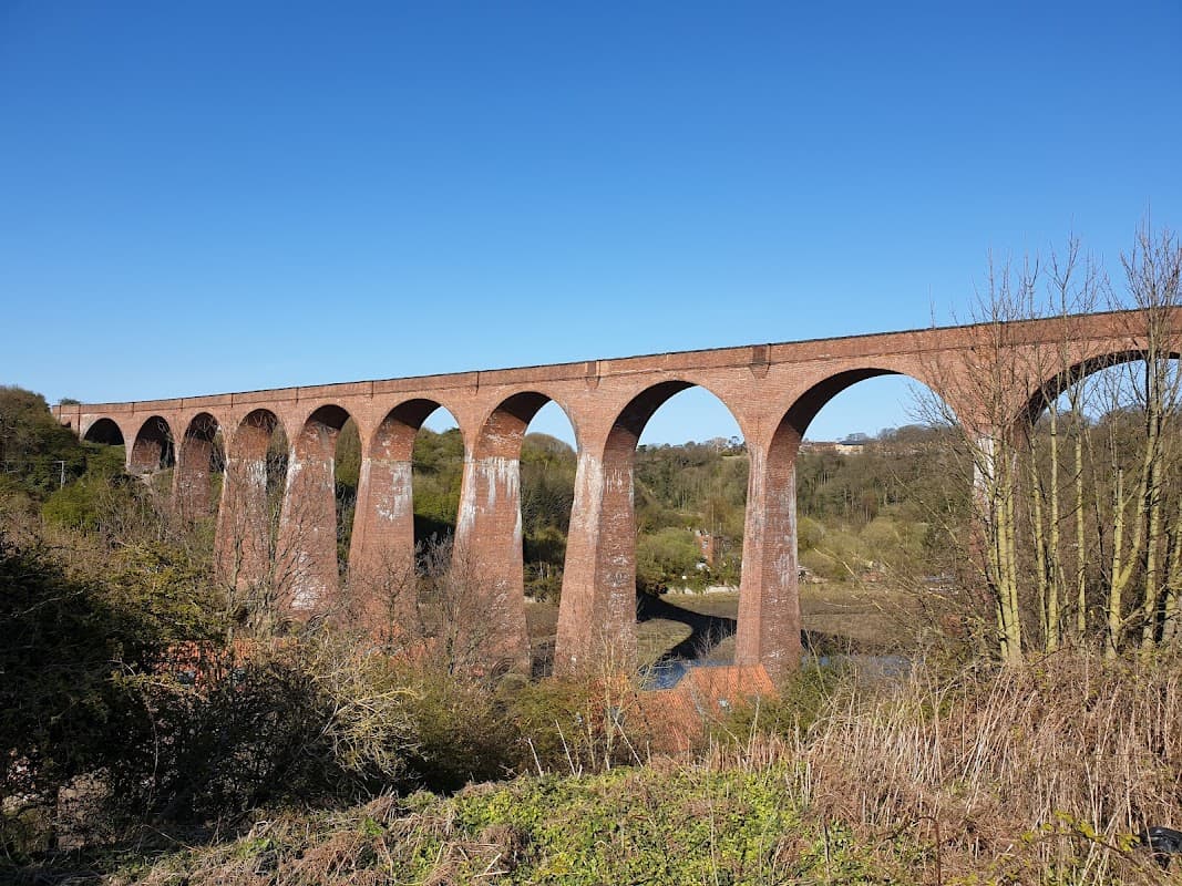 Red brick viaduct arches over a lush valley under a clear blue sky in Ruswarp, Yorkshire.