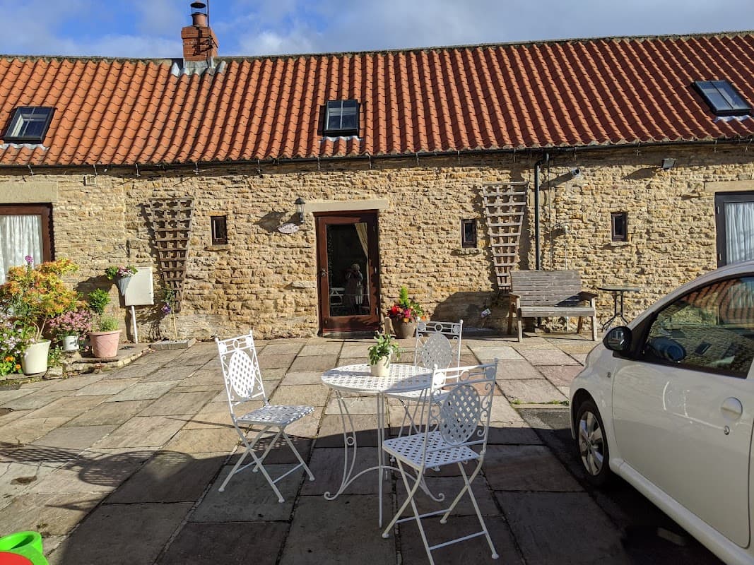 Charming stone cottage with a red-tiled roof, outdoor seating area, and flower pots in a picturesque courtyard.