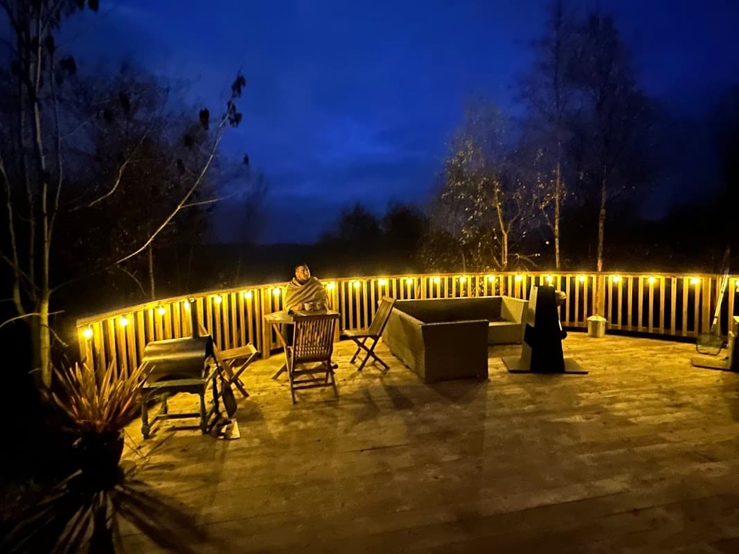 Cozy outdoor deck with warm lighting, seating, and trees under a night sky at Yurtshire Fountains in North Yorkshire.