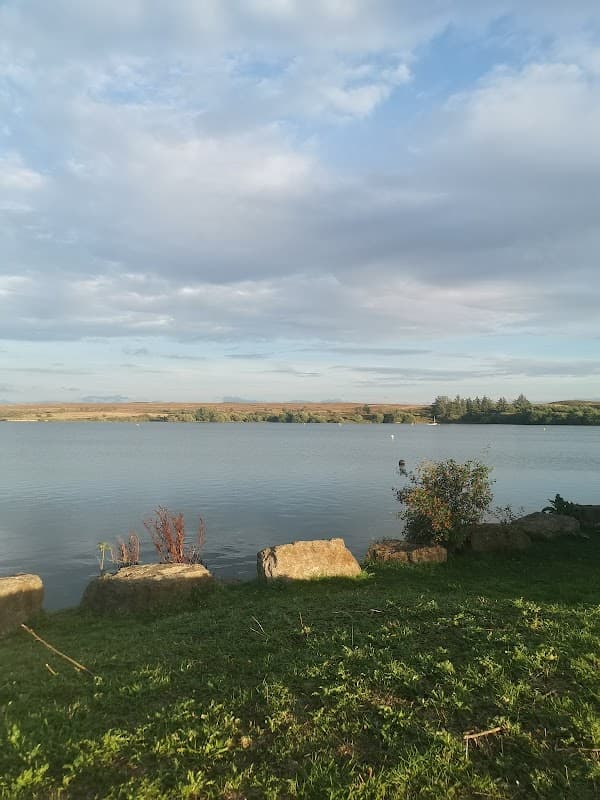 Calm water of Scaling Reservoir surrounded by greenery and rocky outcrops under a partly cloudy sky.