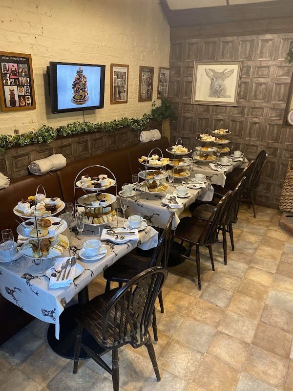 A cozy bakery setting with tables set for afternoon tea, featuring tiered stands of pastries and decorative wall art.