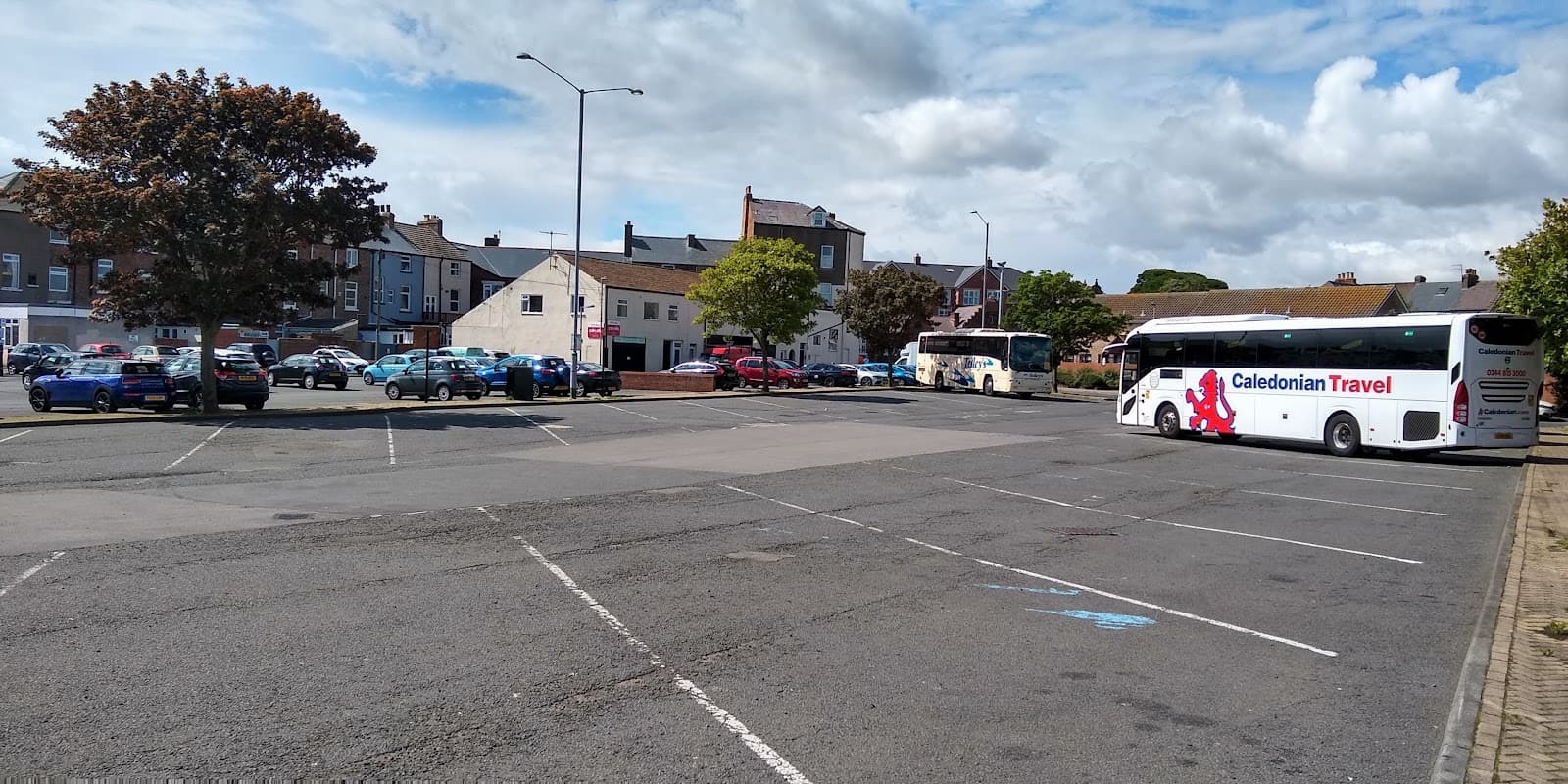 Car and coach park in Scarborough with several parked cars, a bus, and buildings in the background under a cloudy sky.