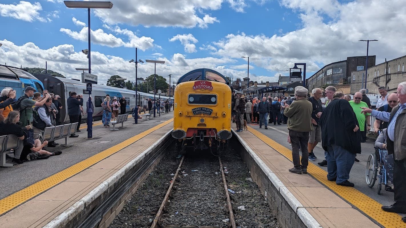 Yellow train at Scarborough Station, with crowds of people on the platform and clear blue skies above.