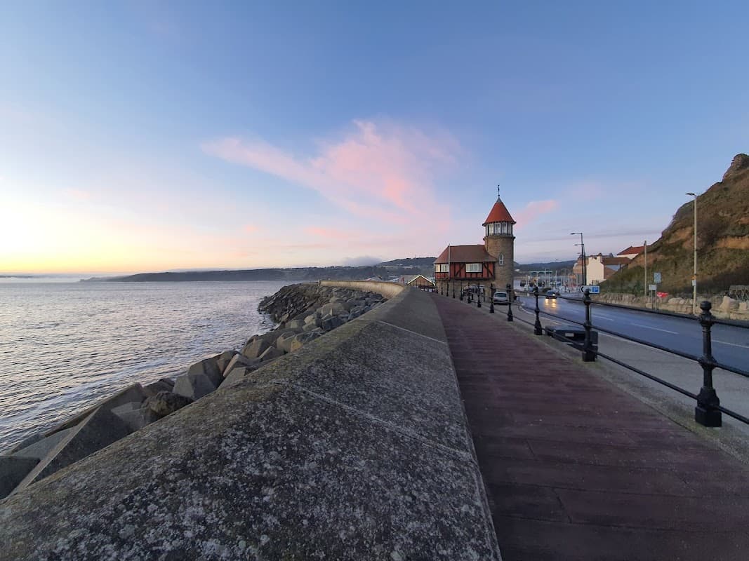 Cleveland Way Parking sign near the coast, with a red-roofed building and rocky shoreline at sunset.