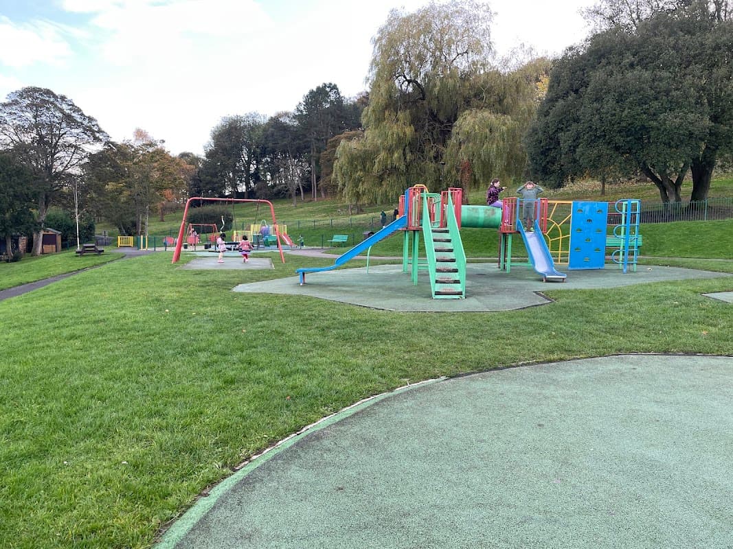 Colorful playground equipment with slides and climbing structures in a grassy park setting. Trees in the background.