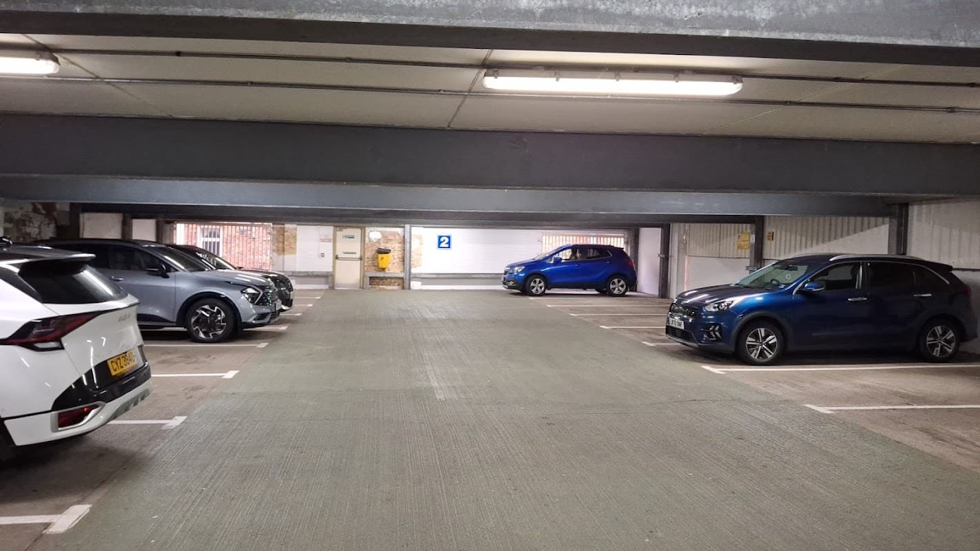 Multi-storey car park with parked cars, including a silver SUV, blue hatchback, and a blue sedan, under fluorescent lights.