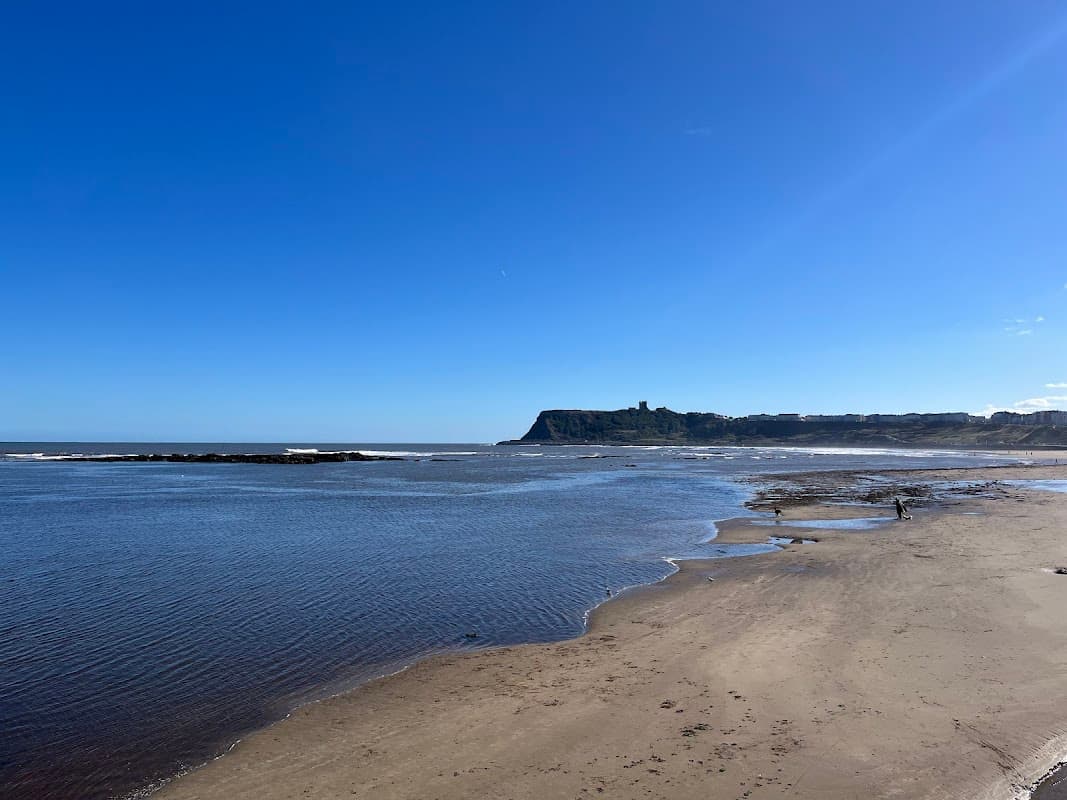 Scenic view of Scalby Mills beach, with calm waters and a clear blue sky, framed by rugged cliffs in the distance.