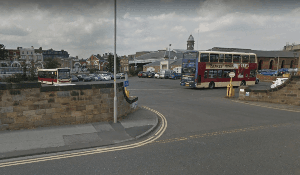A busy car park in Scarborough with parked cars, a bus, and a mix of buildings in the background under a cloudy sky.