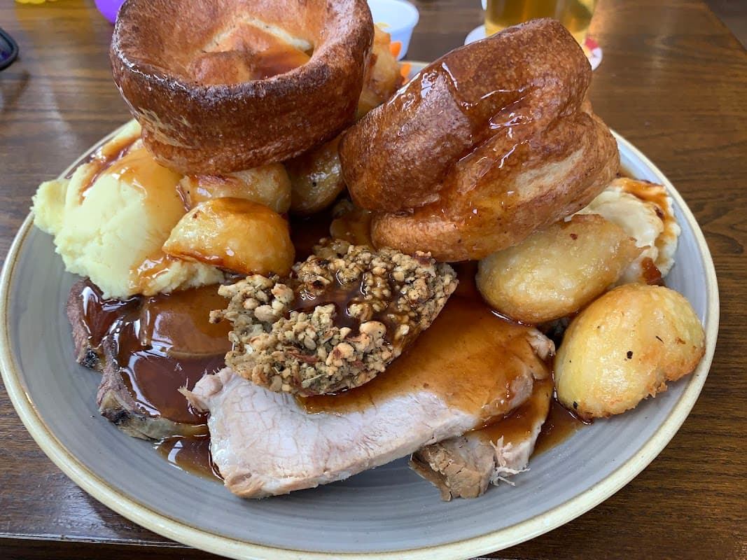 A hearty plate featuring roast beef, Yorkshire puddings, roast potatoes, mashed potatoes, and rich gravy.