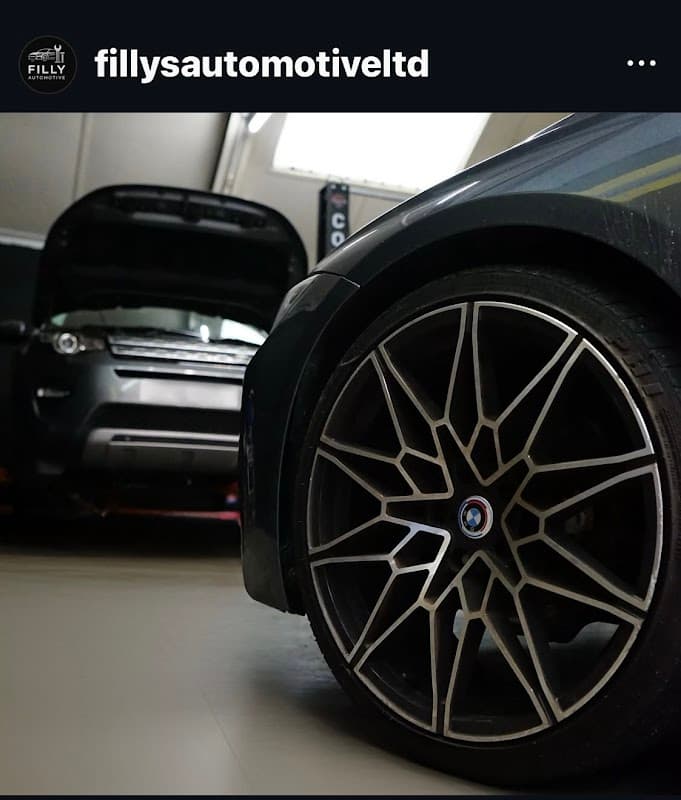 Close-up of a stylish alloy wheel with a blurred car in the background and another vehicle with an open hood.