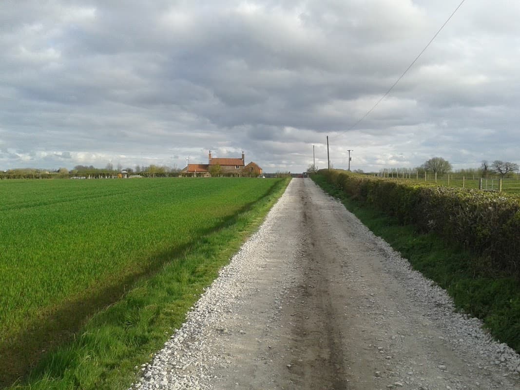 Gravel road leading to Park Farm, surrounded by green fields under a cloudy sky in Scorborough, Yorkshire.