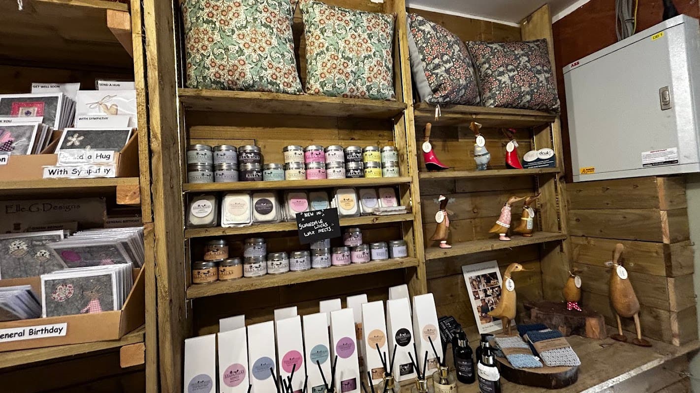 Colorful cushions, candles, greeting cards, and decorative items neatly arranged on wooden shelves at Spring House Farm Shop.