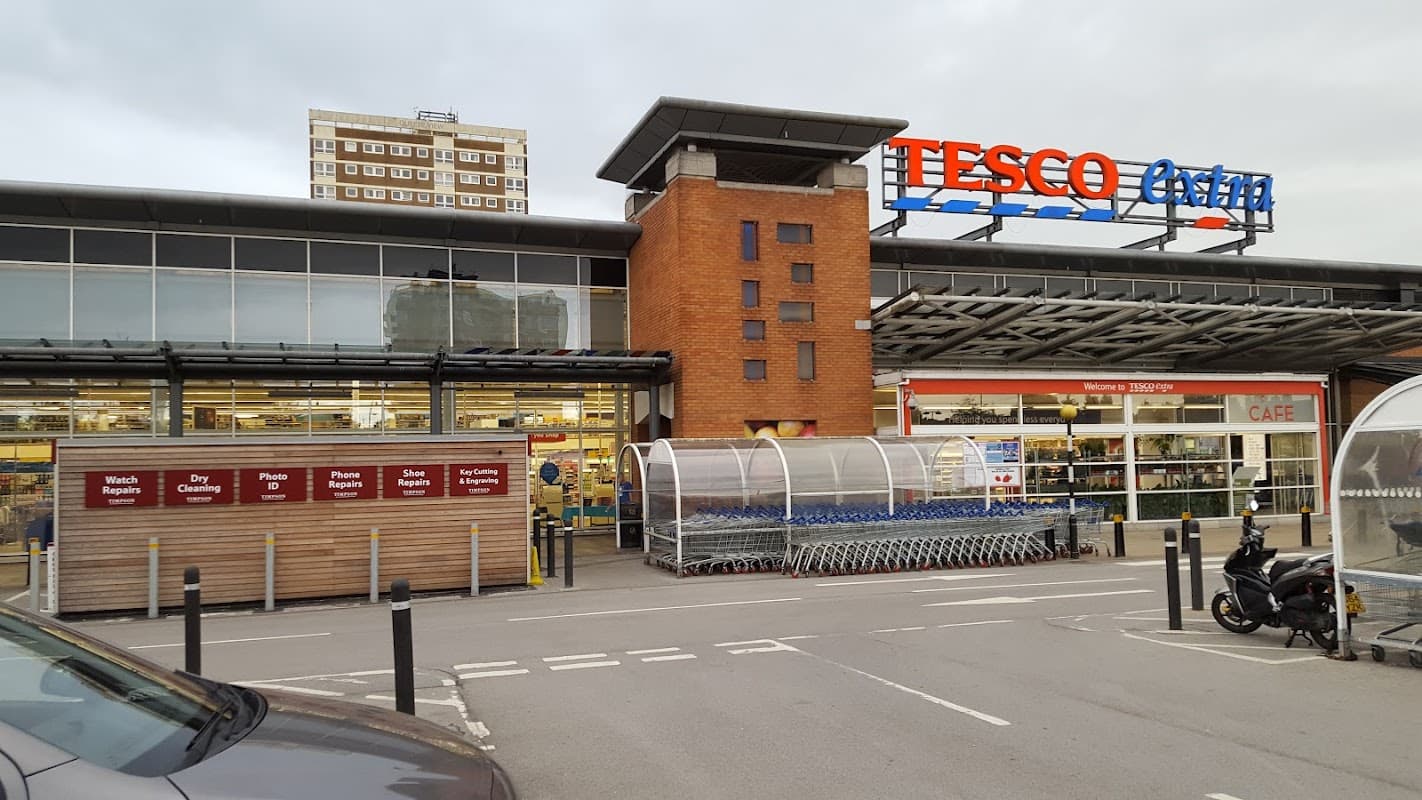 Tesco Extra storefront with shopping carts outside, a café sign, and a residential building in the background.