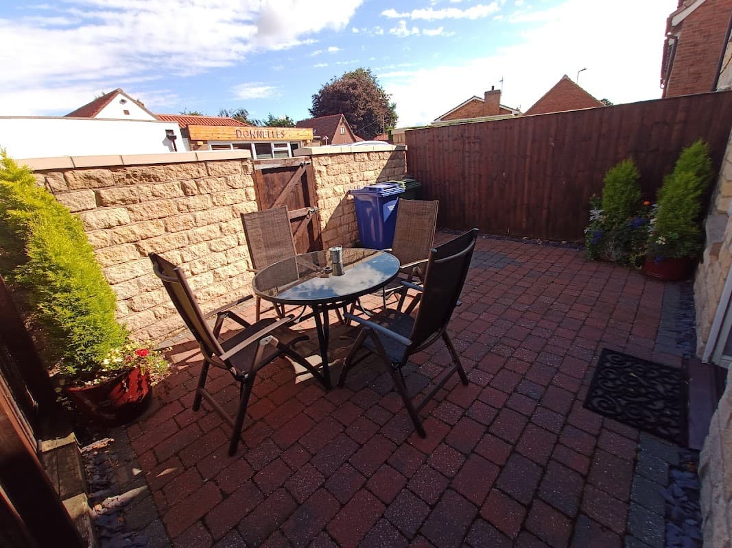 Patio area with a round table and four chairs, surrounded by stone walls and potted plants in Seamer, Scarborough.