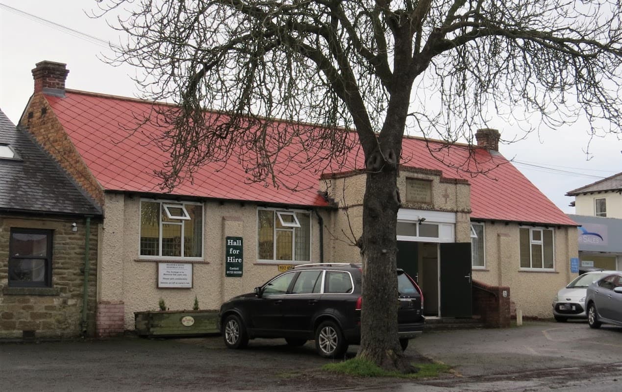 Seamer & Irton Memorial Hall with a red roof, sign reading "Hall for Hire," and surrounding trees and vehicles.
