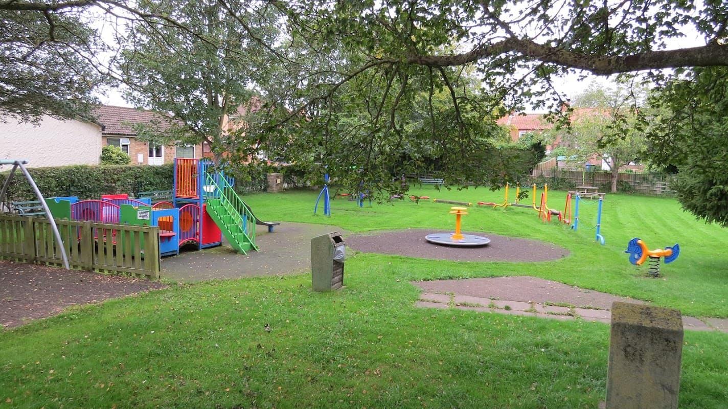 Colorful playground equipment, grassy areas, and benches under trees in a community park.