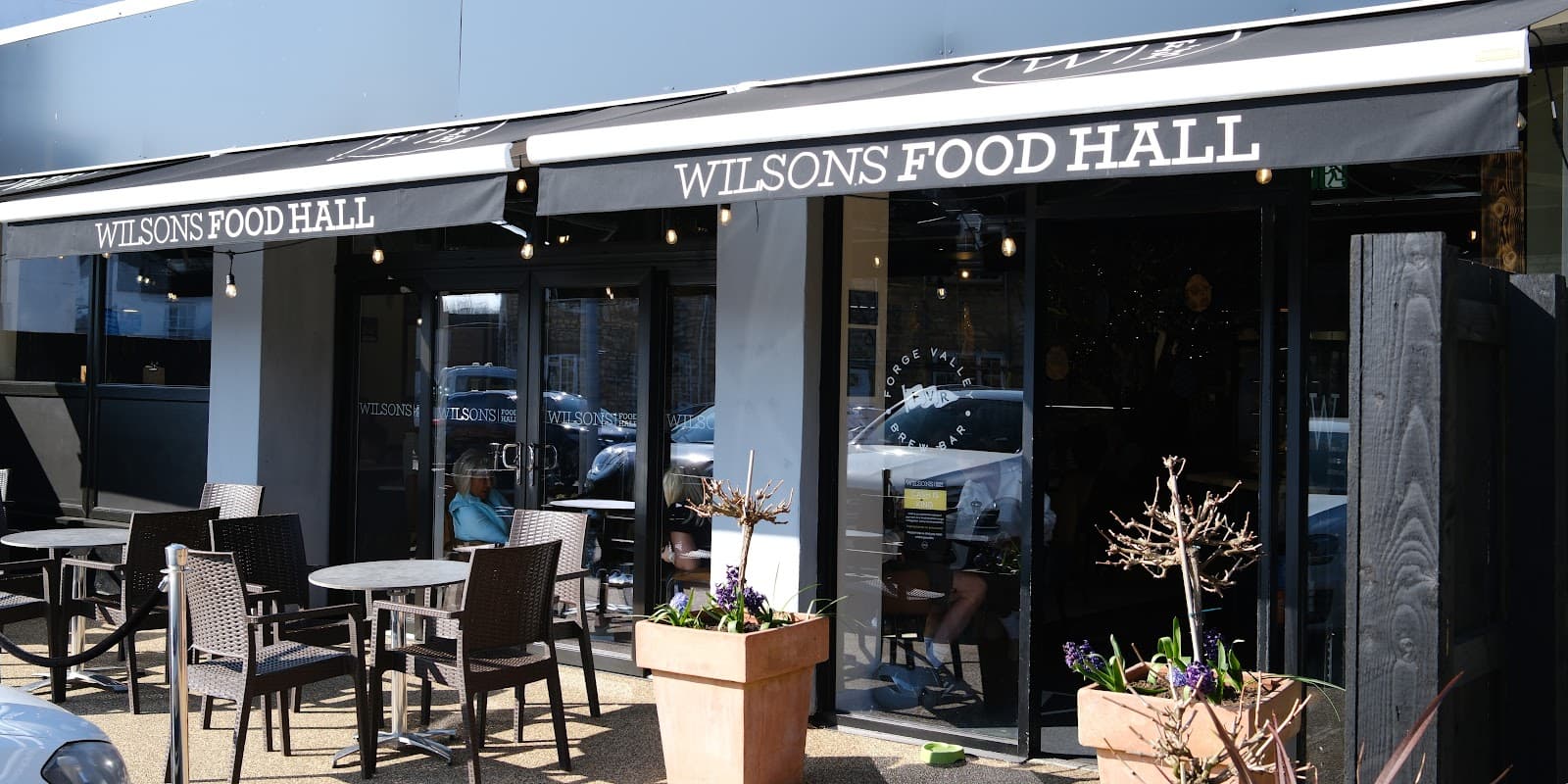 Exterior view of Wilsons Food Hall featuring outdoor seating, planters, and a modern storefront in Seamer, Scarborough.