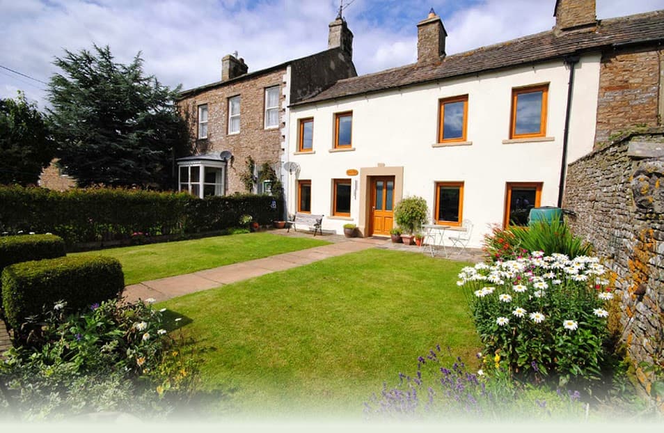 Charming holiday cottage with a well-kept garden, stone walls, and bright orange window frames in Sedbusk, Yorkshire.