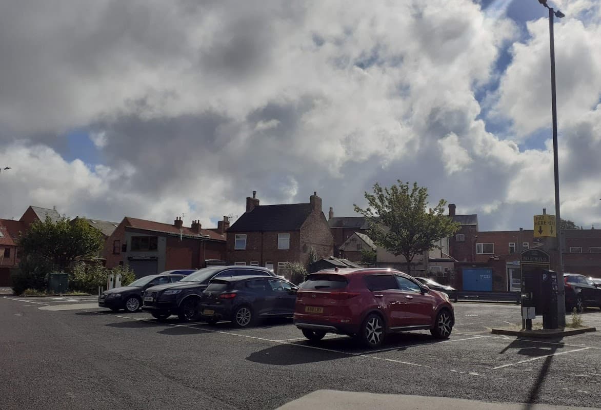 Pay & Display car park with parked cars, buildings, trees, and a cloudy sky in Selby, Yorkshire.