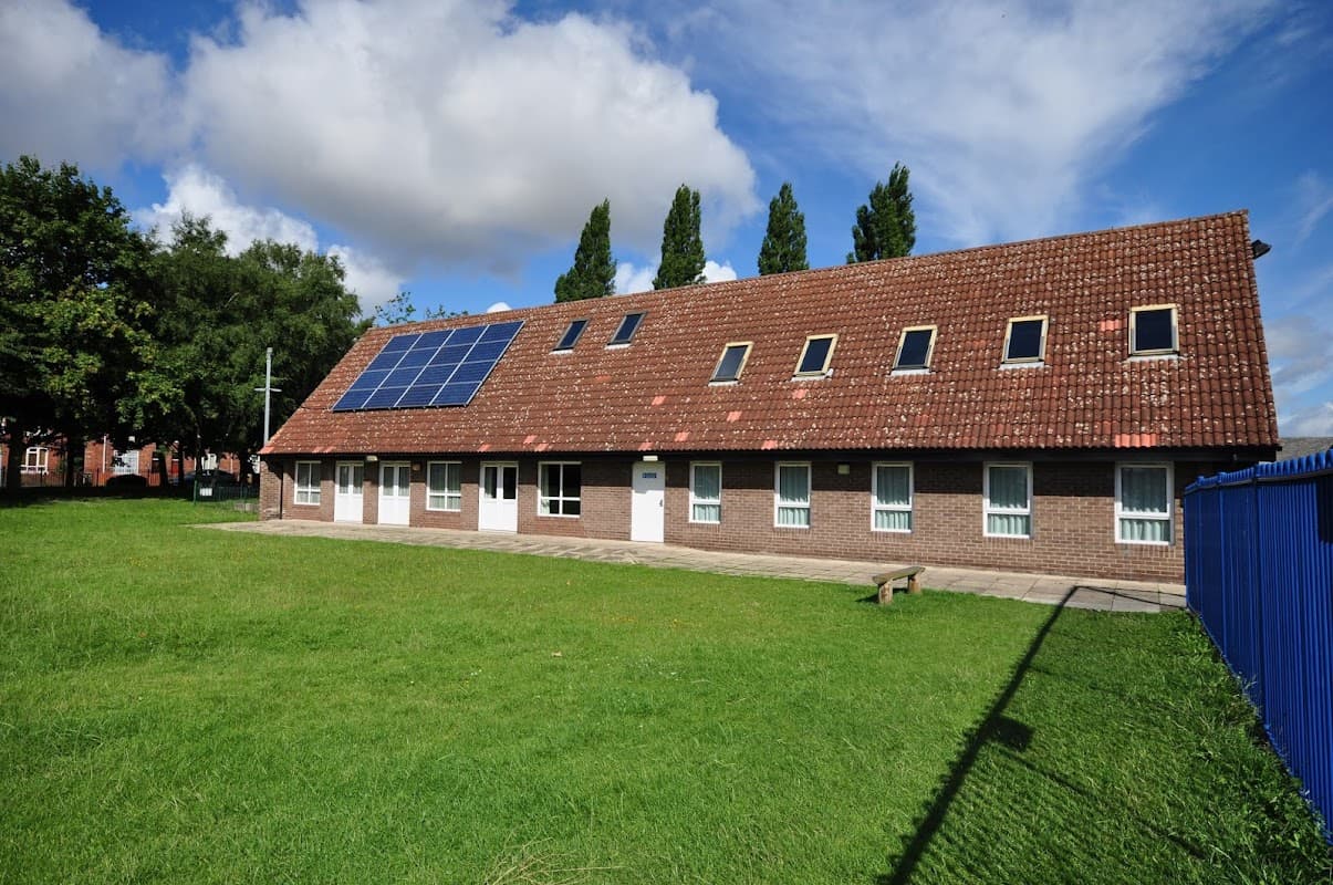 Community center with a sloped roof, solar panels, and green lawn, surrounded by trees and a blue fence.