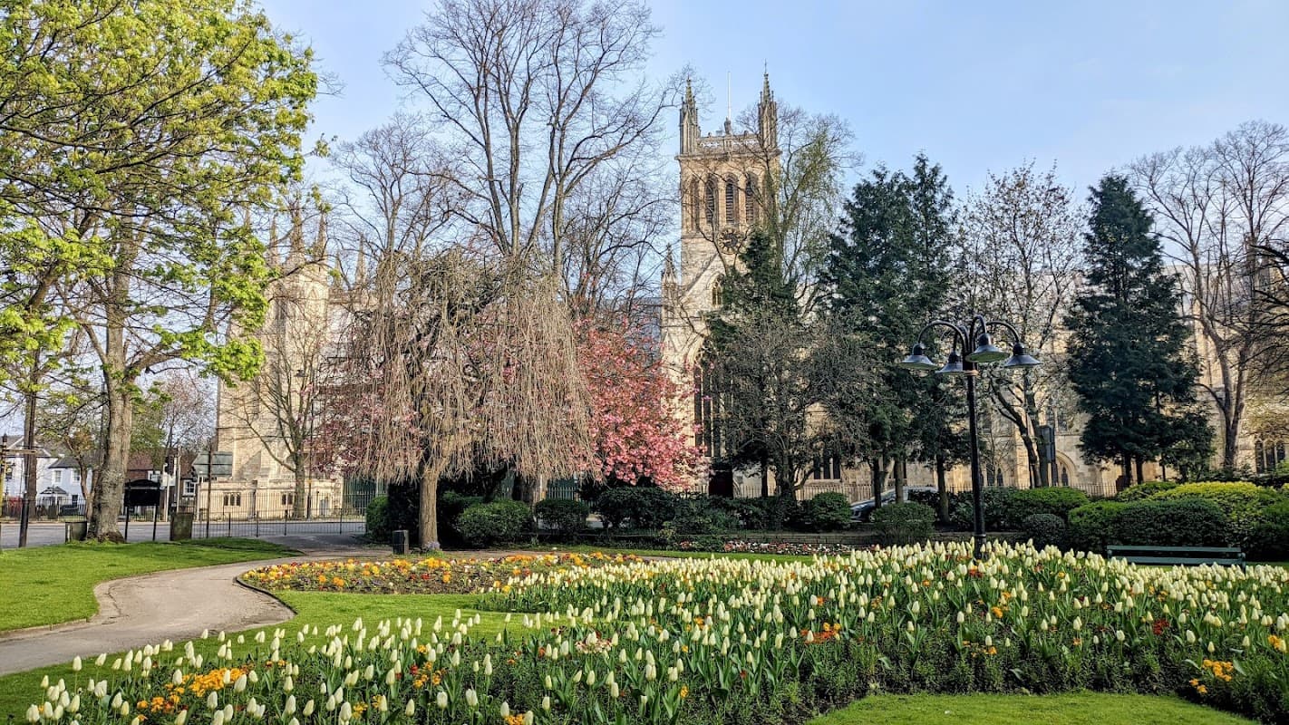 Colorful flower beds in a park with trees and a historic building in the background under a clear blue sky.